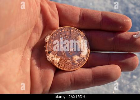 Männliche Hand mit Bitcoin-Kryptokurrency, die aus dem langen Winter schmilzt. Konzept eines stabilen Preises, der gefroren war. Stockfoto