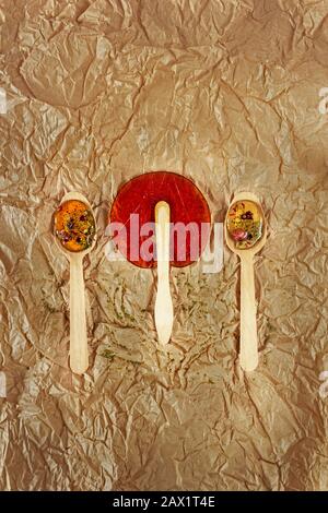 Nützliche Süße. Lutscher werden zu Hause aus natürlichen Zutaten auf Holzlöffeln und einem Stick auf zerknittertem Kraftpapier hergestellt Stockfoto