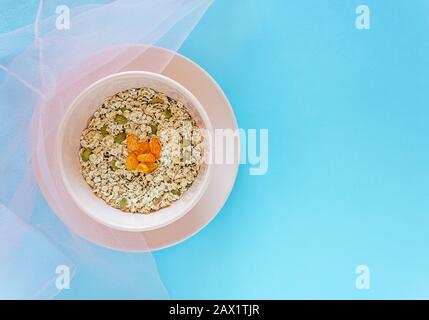 Superfood - Haferflocken in einer rosa Schale mit Chia-Samen, Nüssen, Rosinen mit transparenten, leichten Stofftextilien auf blauem Hintergrund Stockfoto