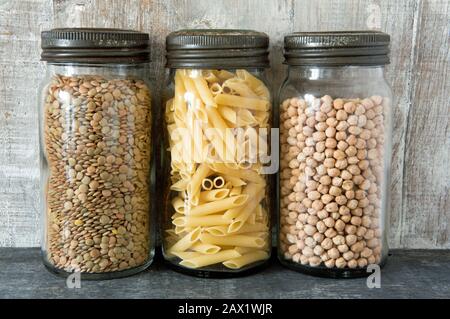 Vintage Glas Kilner Lagerung Lebensmittel Gläser mit Metalldeckel mit Pasta, Linsen und Kichererbsen vor Holzhintergrund in der Küche. Konzept „Keine Verschwendung“ Stockfoto