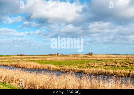 Blick über Nord-Norfolk-Sümpfe von der Gipsy Lane in Titchwell bis zum Clubhaus des Brancassater Golfplatzes in der Ferne an einem hellen Tag im Winter. Stockfoto