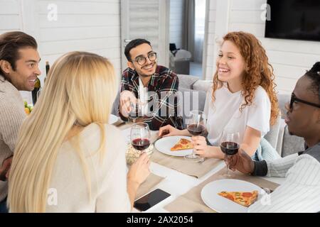Horizontaler Hochwinkelschuss von jungen Männern und Frauen, die während des Essens in einer modernen Wohnung plaudern Stockfoto