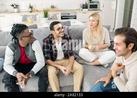 Freunde sitzen auf dem Sofa im modernen Apartment und spielen, Wer Ich bin, mit horizontalem Schuss Stockfoto