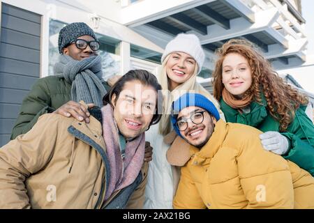 Fünf multiethnische Freunde, die Winterkleidung tragen und dabei lächelnd und horizontal auf die Kamera blicken Stockfoto