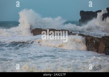 Storm Ciara schlägt die Küste von Cornwall mit riesigen Wellen, die so groß sind wie die umliegenden Klippen, die gegen das Wellenbrecher krachen Stockfoto