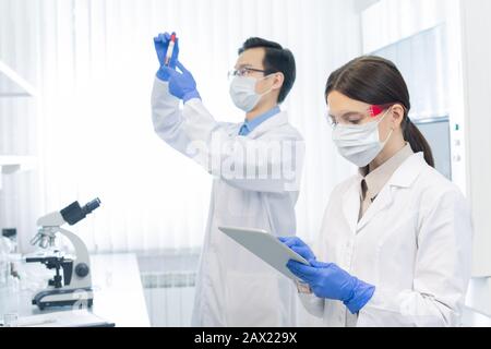 Zwei junge Wissenschaftler tragen Schutzmasken und Handschuhe, die an neuen Medikamenten im modernen Labor arbeiten Stockfoto