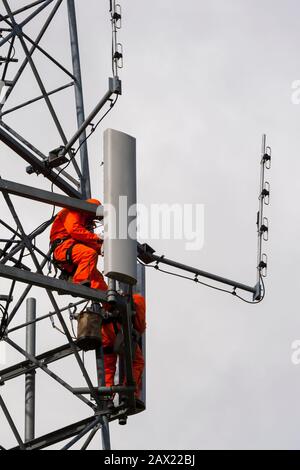 2 Männer tragen orange Overalls Arbeit hoch oben auf einem Radio Turm, Installation und Reparatur von Antennen Stockfoto