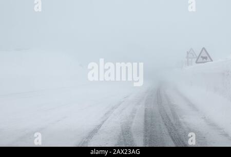 Fahren mit schlechten Sichtverhältnissen auf einer winterlichen, rutschigen Bergstraße mit Schnee und Nebel