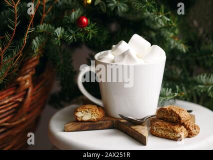 Kaffee in einer weißen Tasse mit Marshmallows. Festlicher Kaffee am Morgen mit traditionellen italienischen Cantuccini-Plätzchen. Kaffeetasse auf grünem Tannenhintergrund B. Stockfoto