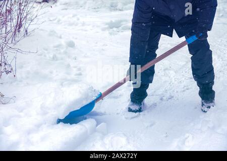 Ein Mann mit Schneeschaufel reinigt im Winter eine Straße. Der Mann schaufelt den Schnee nach einem Schneefall Stockfoto