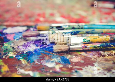 Alte Ölmalbürsten auf befleckter Holzpalette Stockfoto