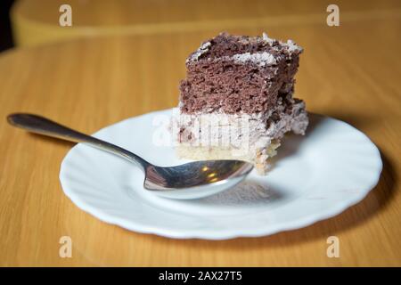Weißer, gehackter Background aus Kuchenteig in einem weißen Teller. Löffel. Brauner und weißer Kuchen auf Holzbrett . Kuchen mit Keks und Sahne. Aus Holz Stockfoto