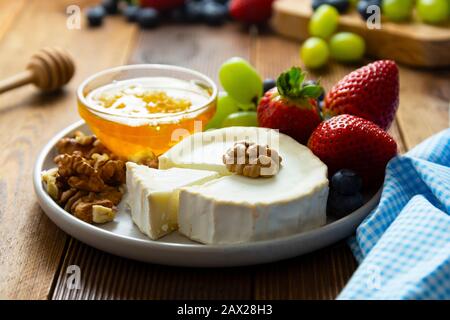 Käseplatte rund geschnittener Weichkäse, Blaubeere, Erdbeere, Trauben und Honig auf Holztisch. Stockfoto