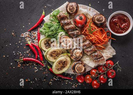 Hühnerkebab mit gegrilltem Gemüse auf einem Holzschneidebrett. Zucchini, grüne Paprika, Tomaten, gegrillte Kartoffeln und Pilze, verschiedene Kräuter, tom Stockfoto