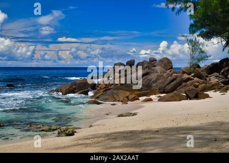 Meereswellen und Granit-Felsen Takamaka Beach, Mahe Island, Seychellen. Palmbäume, Sand, abstürmende Wellen, schönes Ufer, blauer Himmel und türkisfarbenes Wasser
