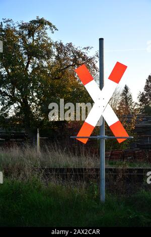 Andrews Kreuz vor den Schienen mit Baum, Gras und Wald Stockfoto