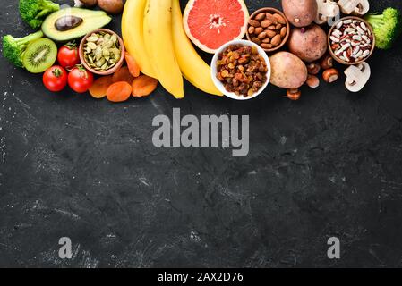 Die Nahrung enthält natürliches Kalium. K: Kartoffeln, Pilze, Banane, Tomaten, Nüsse, Bohnen, Brokkoli, Avocados. Draufsicht. Auf schwarzem Hintergrund. Stockfoto