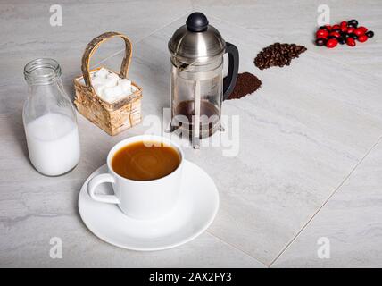 Hochwinkeliger Blick auf Kaffeebeeren, Bohnen und Boden auf der Theke mit einer Tasse frisch gebrühtem französischen Presskaffee. Stockfoto