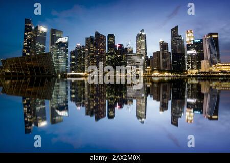 Die Skyline der Stadt Singapur am Abend zeigt Bürogebäude im Finanzviertel, die sich auf dem Wasser niederschlugen. Stockfoto