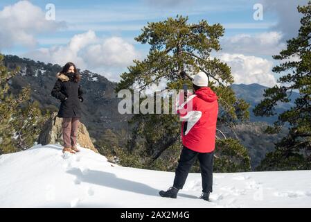 Zwei junge, glückliche Teenager fotografieren mit einem Handy auf einem verschneiten Berg. Troodos Berge Zypern Stockfoto