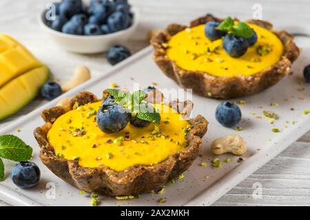 Vegane Rohmango-Käsekuchen mit frischen Beeren, Minze und Nüssen. Gesundes veganes glutenfreies Speisekonzept. Nahaufnahme Stockfoto