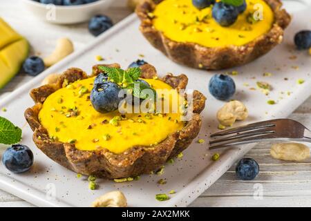 Gelbe Mango vegane Rohkuchen mit Blaubeeren, Minze und Nüssen. Gesunde köstliche Speisen. Nahaufnahme Stockfoto