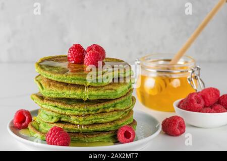 Matcha-Tee-grüne Pfannkuchen. Haufen hausgemachter Pfannkuchen mit frischen Himbeeren und Honig. Gesundes Frühstücksdessert. Nahaufnahme Stockfoto