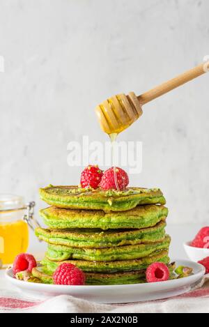 Hausgemachte Pfannkuchen mit Matcha-Tee, frischen Himbeeren und fließendem Honig. Gesundes Frühstücksdessert. Vertikale Ausrichtung Stockfoto