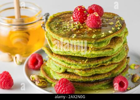 Hausgemachte Pfannkuchen mit Matcha-Tee, frischen Himbeeren, Pistazien und Honig. Gesundes Frühstücksdessert. Nahaufnahme Stockfoto