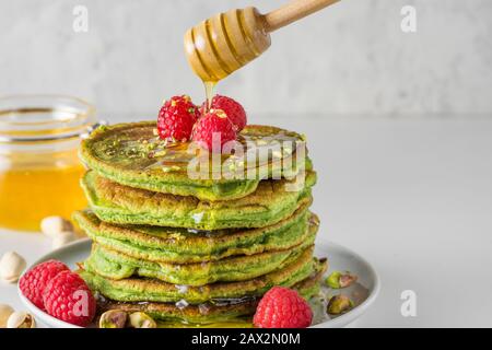 Matcha-Tee-grüne Pfannkuchen. Haufen hausgemachter Pfannkuchen mit frischen Himbeeren, Pistazien und fließendem Honig. Gesundes Frühstücksdessert Stockfoto