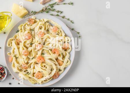 Italienische Nudeltagliatelle mit Garnelen in cremiger Soße mit Parmesankäse und Thymian auf einem Teller auf weißem Marmortisch. Draufsicht mit Kopierraum Stockfoto