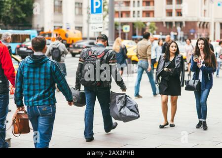 Moskau, Russland - 7. JULI 2017. Ein Motorradfahrer mit einem Schutzhelm in der einen Hand und einem Motorradkoffer in der anderen Hand geht entlang einer belebten Straße Stockfoto