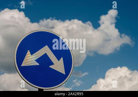 Blaues Verkehrszeichen mit zwei Pfeilen für zwei Richtungen in der Nähe auf weißem Wolken blauem Himmel Hintergrund Stockfoto
