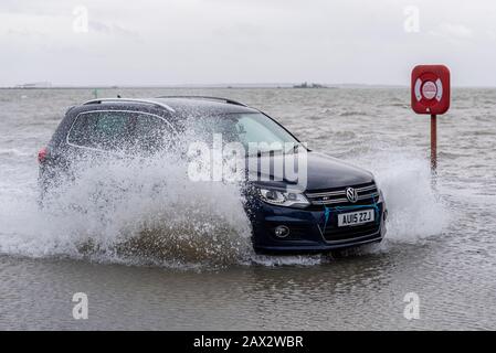 VW-Auto fährt bei Flut und stürmischem Wetter in Southend on Sea, Essex, Großbritannien mit Geschwindigkeit durch Flutwasser. Korrosiver Salzwasser. Rettungsgurt Stockfoto