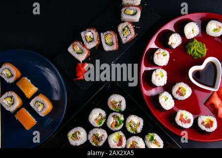 Brötchen verschiedener Art werden auf verschiedenen Platten zusammen mit Sojasoße, Wasabi- und Sushi-Stöcken ausgelegt, die Platten stehen auf schwarzem Grund Stockfoto