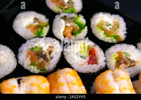 Brötchen und Mohn liegen in der Nähe von Lachs, Garnelen, Avocado, Gurken und Algen. Stockfoto