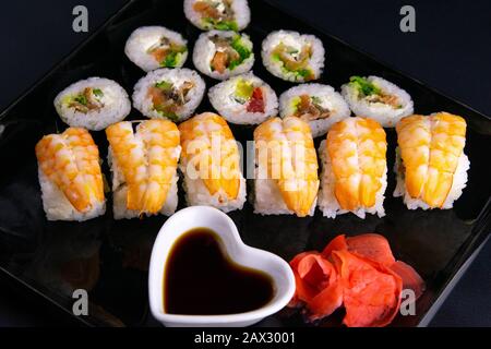 Brötchen und Mohn liegen in der Nähe mit Lachs, Garnelen, Avocado, Gurken, Algen auf schwarzem Teller. Stockfoto