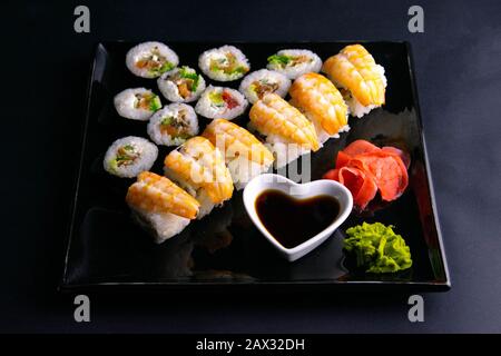 Brötchen und Mohn liegen in der Nähe mit Lachs, Garnelen, Avocado, Gurken, Algen auf schwarzem Teller. Stockfoto