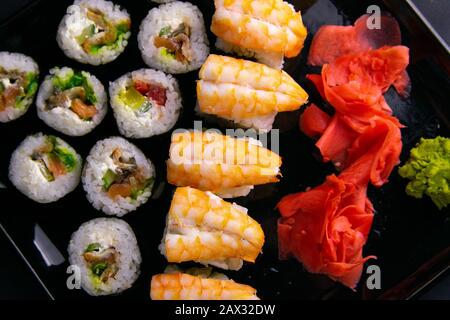Brötchen und Mohn liegen in der Nähe mit Lachs, Garnelen, Avocado, Gurken, Algen auf schwarzem Teller. Stockfoto