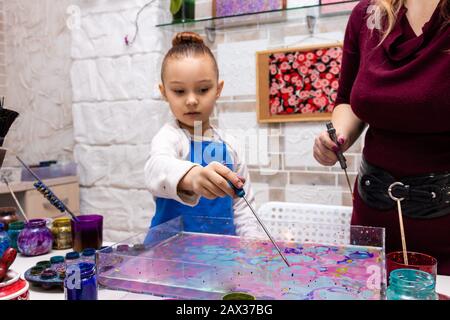 Die Lehrerin zeigt die Techniken des Mädchens, um Gemälde zu erstellen. Meisterklasse im Atelier Ebru - die Kunst des "Malens auf dem Wasser". Stockfoto