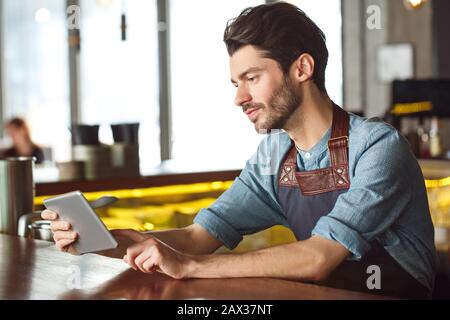 Beruf. Barkeeper lehnt sich freudig an das Gegenspiel auf dem digitalen Tablet an Stockfoto