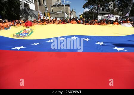 10. Februar 2020, Venezuela, Caracas: Orangefarbene Regierungsbefürworter tragen eine riesige venezolanische Flagge aus Protest gegen die Ankündigung neuer Sanktionen gegen die venezolanische Fluggesellschaft Conviasa, deren Logo orange ist, durch die USA. "Die staatliche Fluggesellschaft Conviasa unterstützt das illegale Regime Maduros durch Flüge von Beamten seines korrupten Regimes auf der ganzen Welt", zitierte das US-Finanzministerium Finanzminister Mnukhin bei der Ankündigung neuer Sanktionen. "Wir werden an internationale Gerichte appellieren", konterte der venezolanische Staatschef Maduro während des Protests vor zahlreichen Anhängern Stockfoto