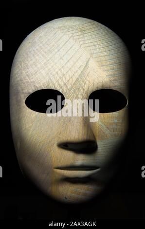 Strukturierte Maske mit Risse im rauhen Holz lackiert, neutralen Ausdruck auf dunklem Hintergrund. Stockfoto