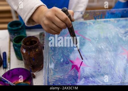 Meisterklasse im Atelier Ebru - die Kunst des "Malens auf dem Wasser." Kinderhand schafft ein Muster auf dem Wasser mit der Ebru-Technik Stockfoto
