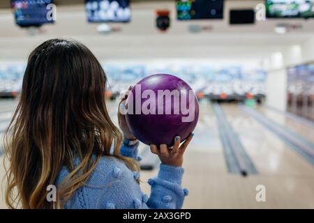 Bowlingspiel. Frau hat Spaß beim Bowling im Club. Mädchen, die den Ball bereit halten, ihn zu werfen und auf den Bildschirm zu schauen Stockfoto