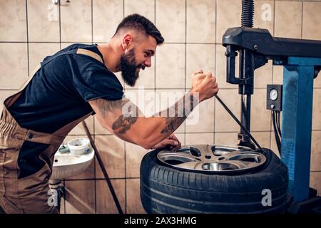 Professioneller Automechaniker beim Reifenwechsel in der Kfz-Werkstatt.Automechaniker beim Reifenwechsel an der Felge in der Garage. Stockfoto