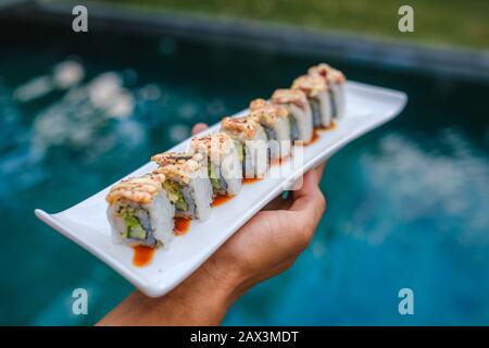 Halten Sie ein Tablett mit Sushi vor dem Pool Stockfoto