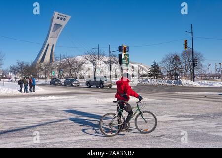 Montreal, CA - 8. Februar 2020: Mann, der im Winter mit dem Fahrrad vor dem Olympiastadion Montreal fährt Stockfoto