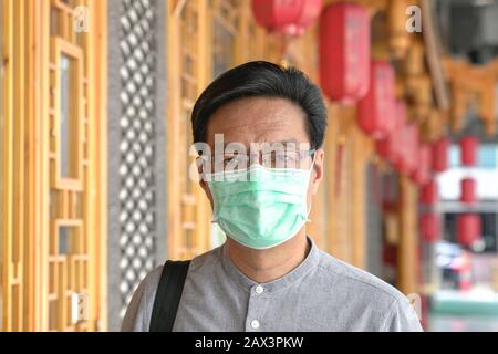 Portrait des asiatischen Chinesen, der eine chirurgische Gesichtsmaske trägt. Schutz vor Viren oder Dunst im Außenbereich. Stockfoto