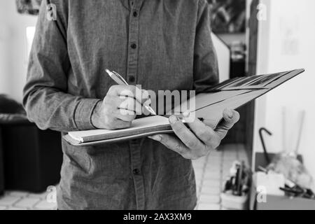 Nahaufnahme und selektive Fokussierung auf die Hände des Menschen, während er einen Stift hält und Notizen auf ein Notizbuch mit Lederkartenabdeckung in Schwarzweiß schreibt Stockfoto